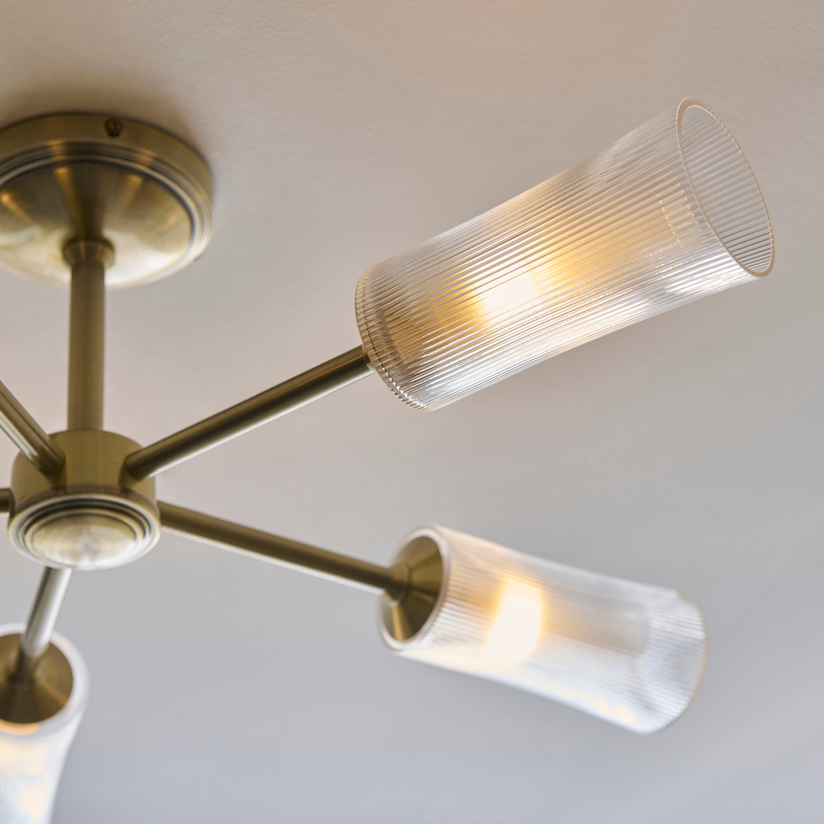 Avelyn semi flush light viewed from below, ribbed glass shades glowing on brass arms