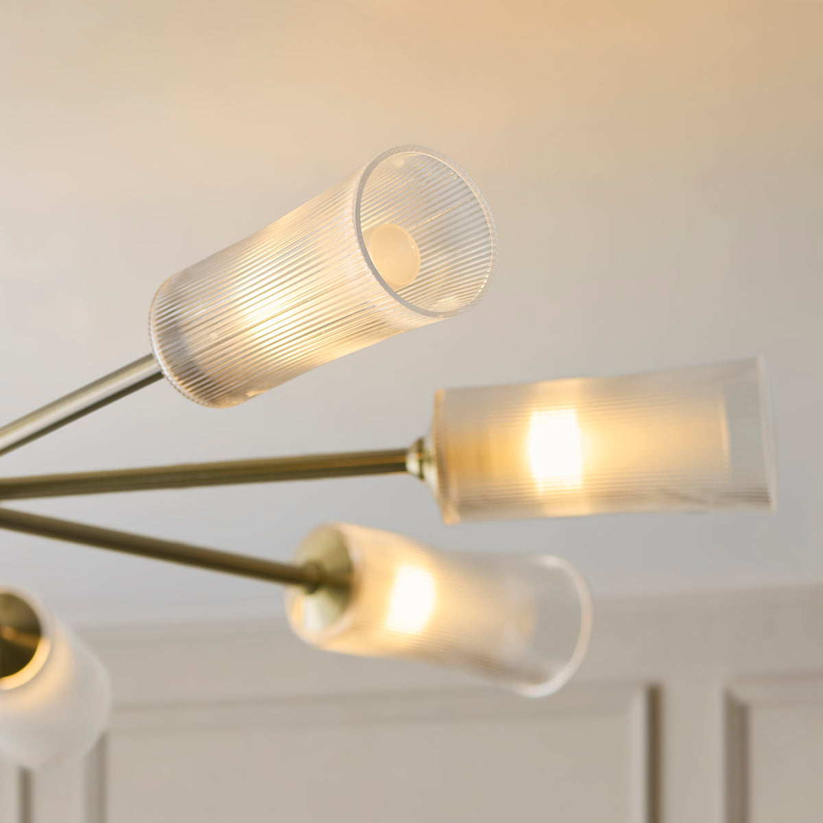 Close-up of two Avelyn brass arms with clear ribbed glass shades and lit bulbs