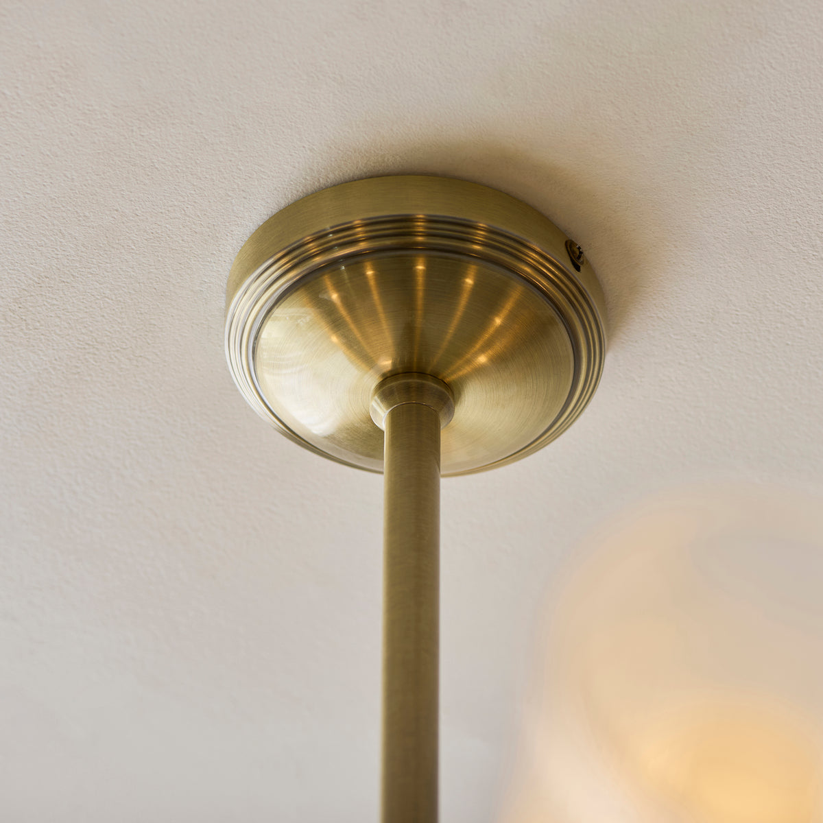 Antique brass ceiling plate and stem of the Avelyn chandelier against a white ceiling