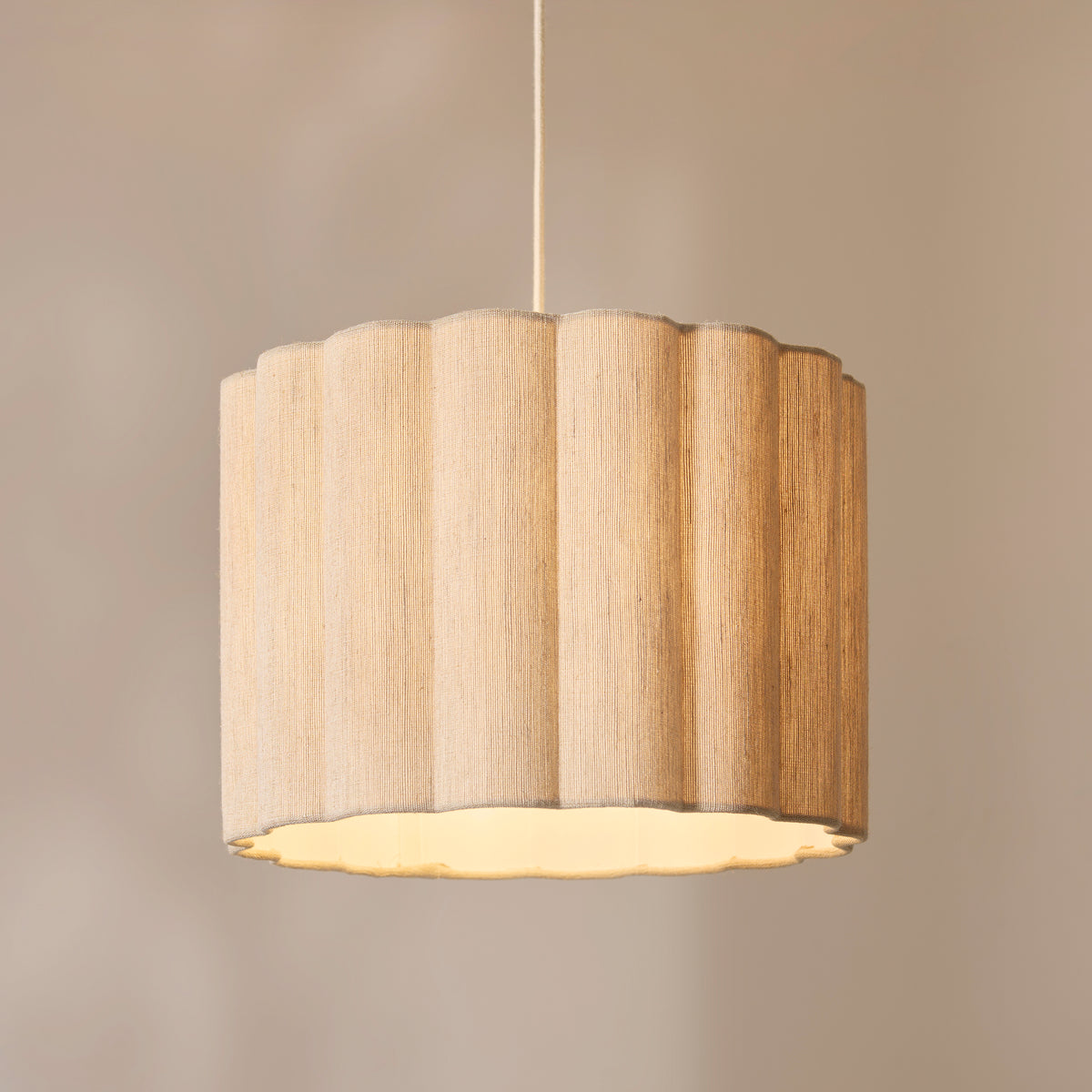Olson pendant's scalloped natural fabric drum shade lit against a warm neutral wall