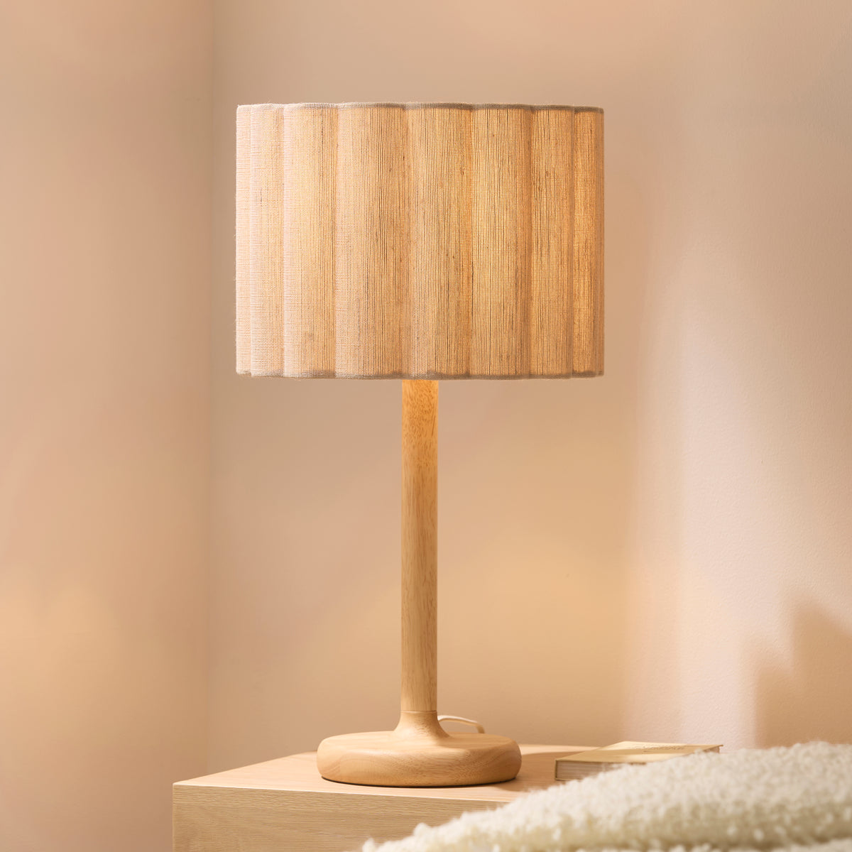 Olson table lamp glowing warmly on a pale wooden bedside surface against a soft neutral wall