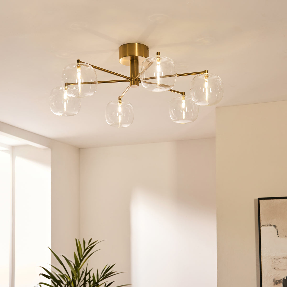 Oslo brass semi flush ceiling light glowing in a bright corner room with tall windows