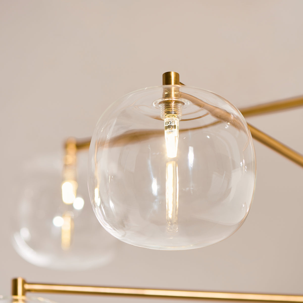 Detail of one clear glass globe shade and filament bulb on the Oslo brass pendant