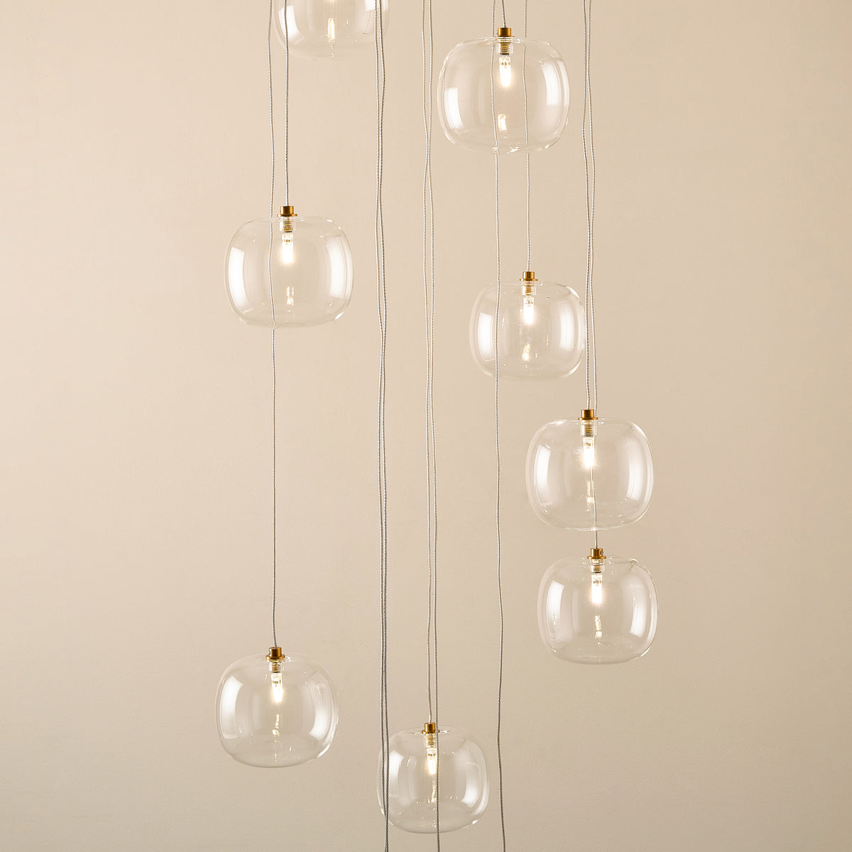Clear glass globe shades of the Oslo cascade pendant hanging at staggered heights on slim cables
