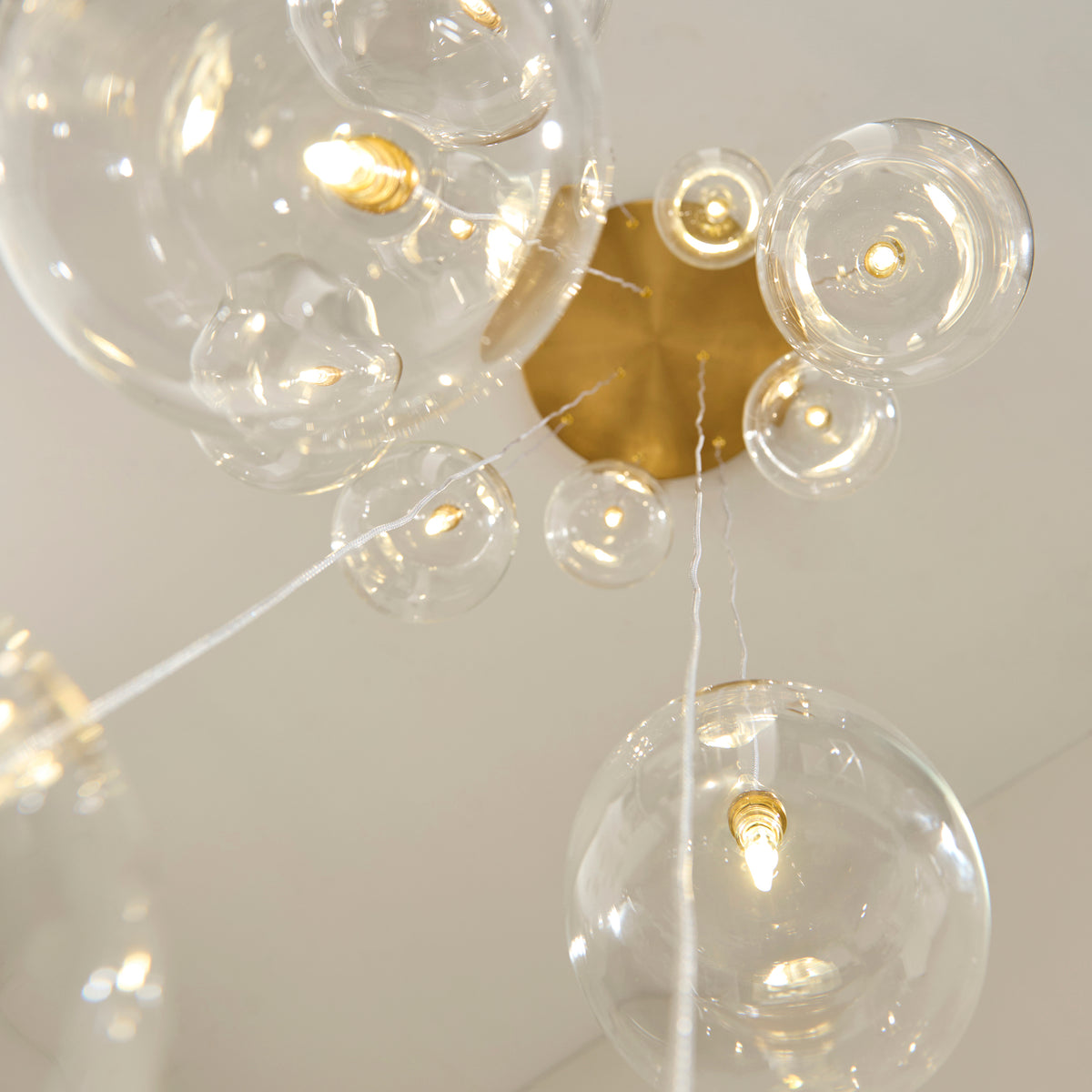 Brushed brass ceiling plate of the Oslo cascade pendant with clear glass globes suspended below