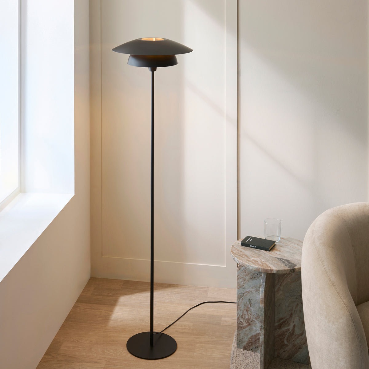 Lyon layered floor lamp glowing next to a boucle armchair by a sunlit window