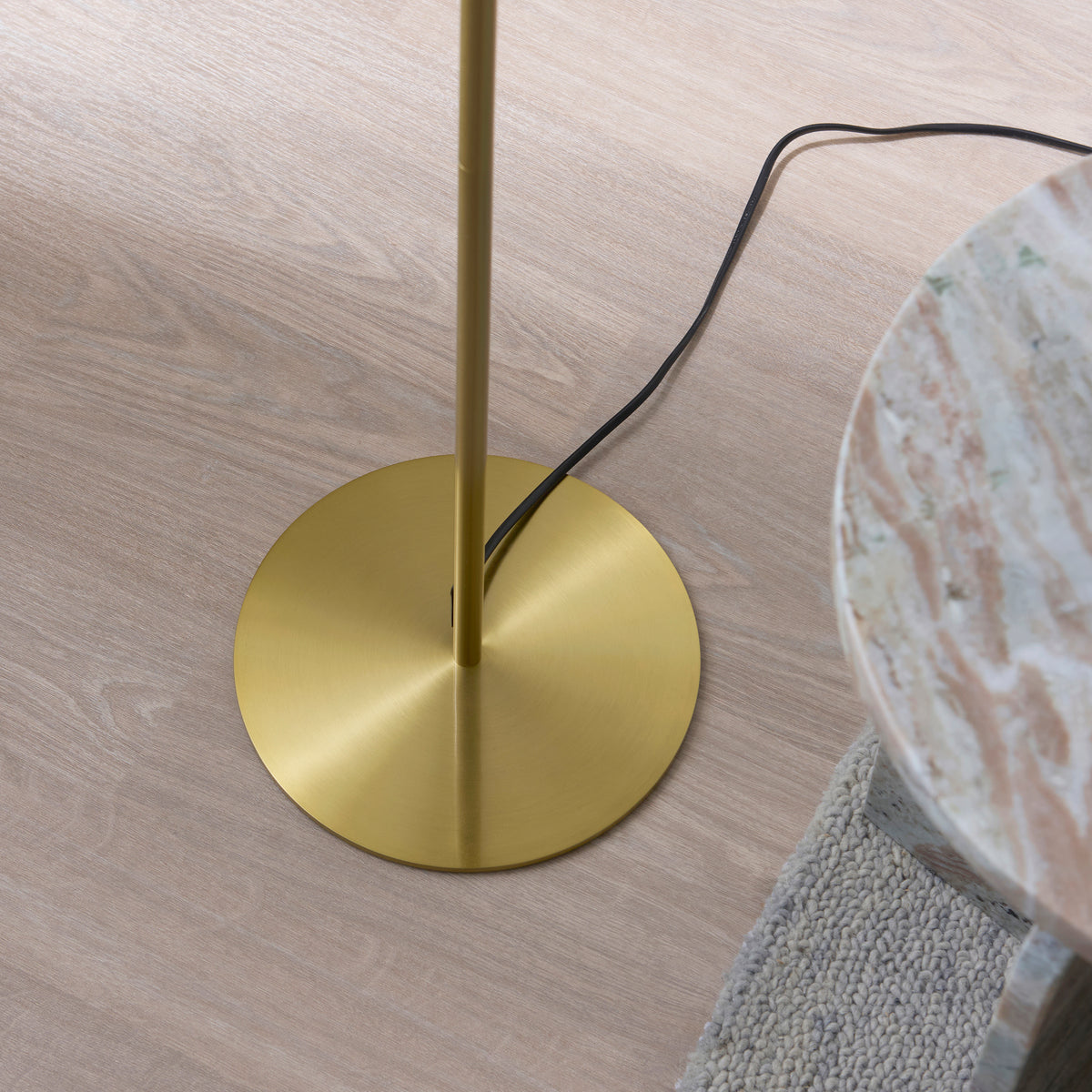 Brushed brass disc base and stem of the Lyon floor lamp on oak flooring