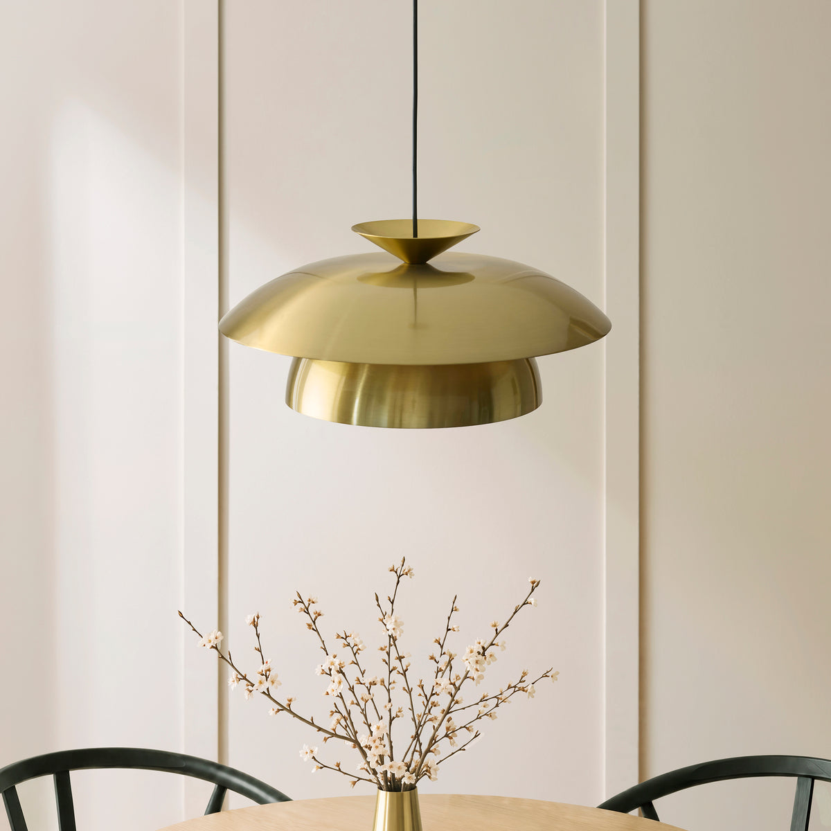 Lyon brass pendant hanging above a dining table with a tall blossom arrangement