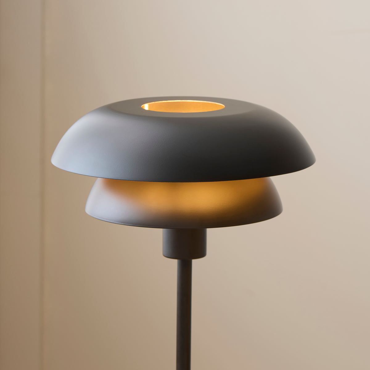 Layered matt black shades of the Lyon table lamp lit softly against a pale wall