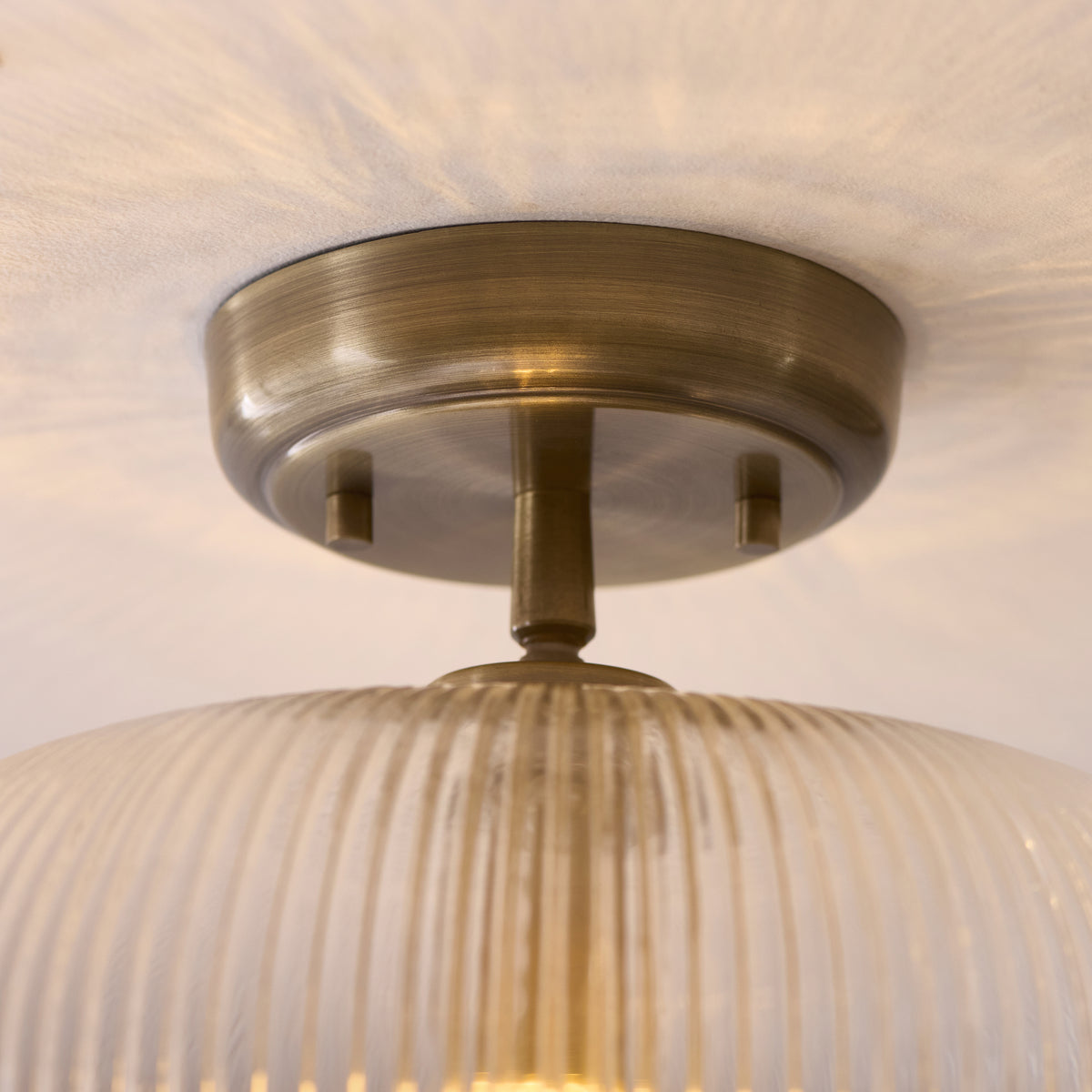 Detail of the Harborne flush light's antique brass ceiling plate and ribbed glass rim