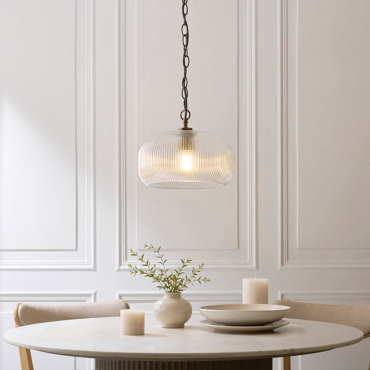 Clear ribbed glass Harborne pendant glowing over a marble dining table set with bowls and a stone vase