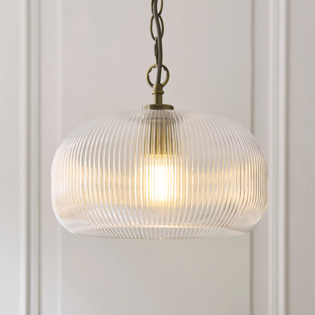 Close view of the Harborne pendant's clear ribbed glass dome and antique brass fitting with lit bulb