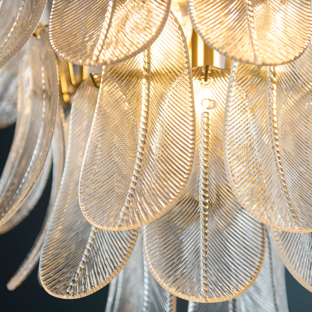 Close-up of ribbed clear glass leaf plates and brass arms inside the lit Autumn chandelier