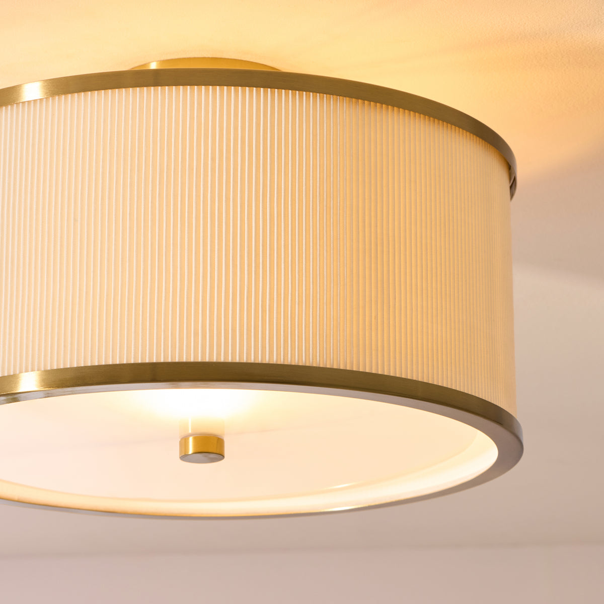 Angled close-up of the Lexi flush light's pleated ivory shade, brass rims and glass diffuser