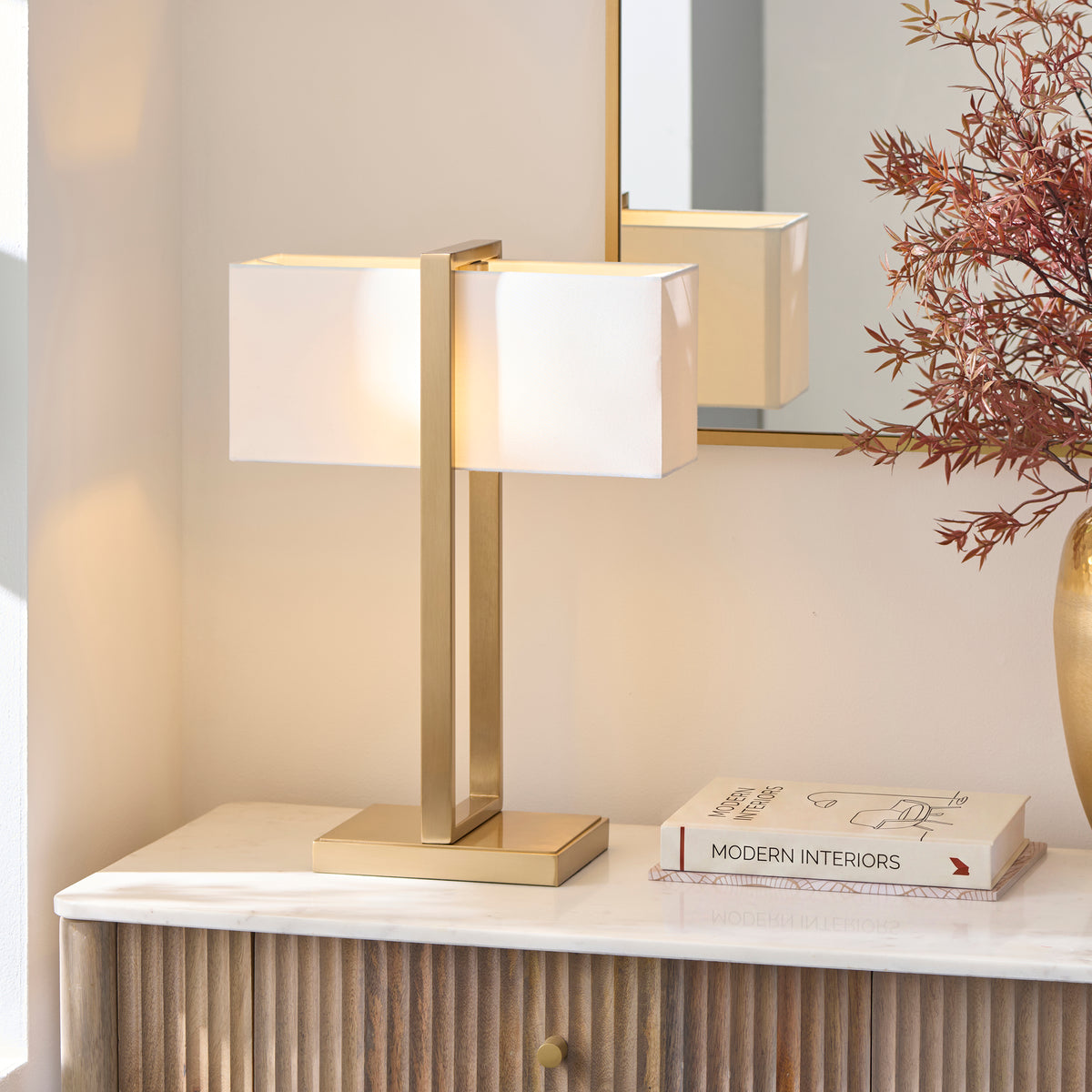 Seattle brass table lamp lit on a marble console with a gold vase, books and wall mirror behind