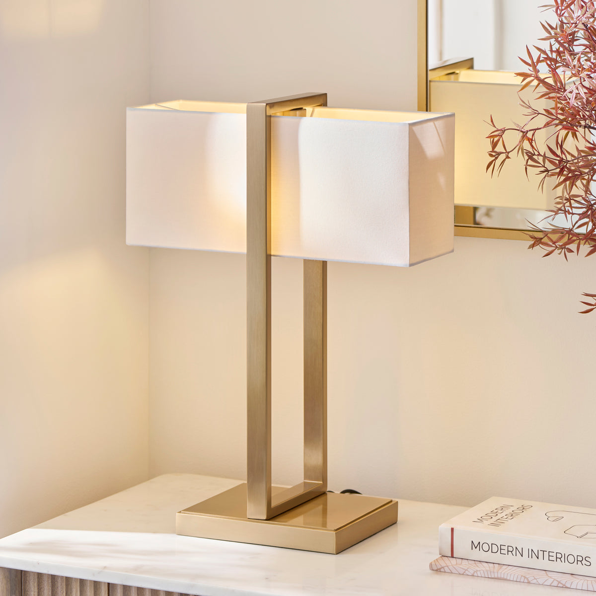 Seattle table lamp's ivory rectangular shades glowing against a marble console and gilt-framed mirror