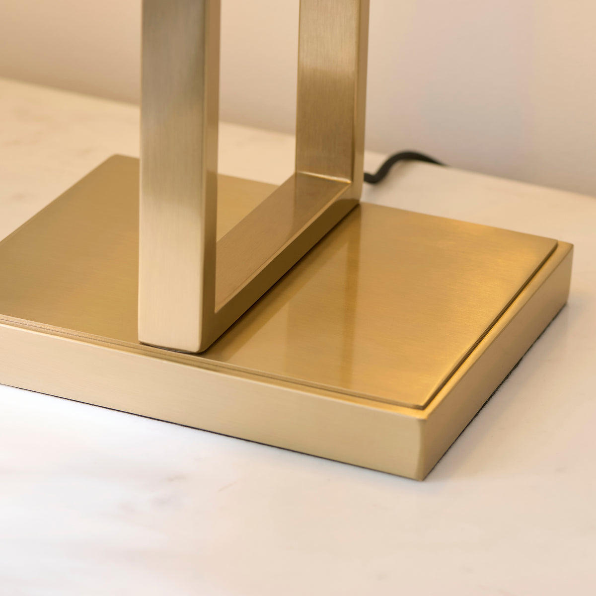 Close-up of the Seattle table lamp's stepped brushed brass square base on a marble surface