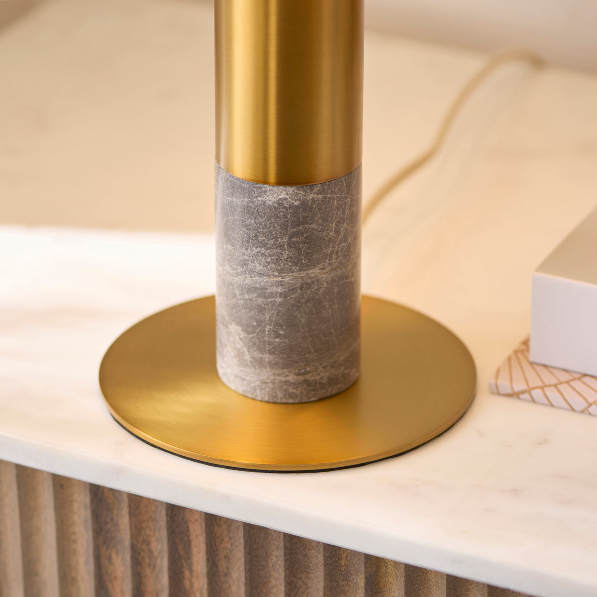 Close-up of the Hansel lamp's grey marble column and brushed brass disc base on marble