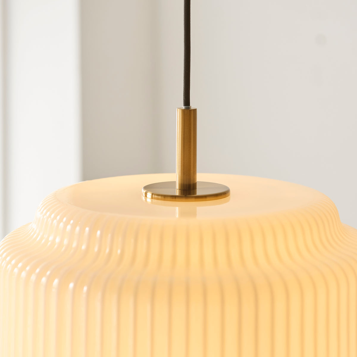 Close-up of the Evora pendant's aged brass stem and disc atop the ribbed opal glass shade