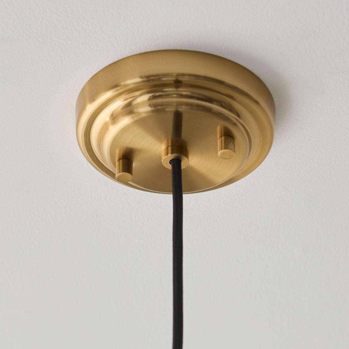 Aged brass ceiling rose of the Evora pendant with black fabric flex against a white ceiling