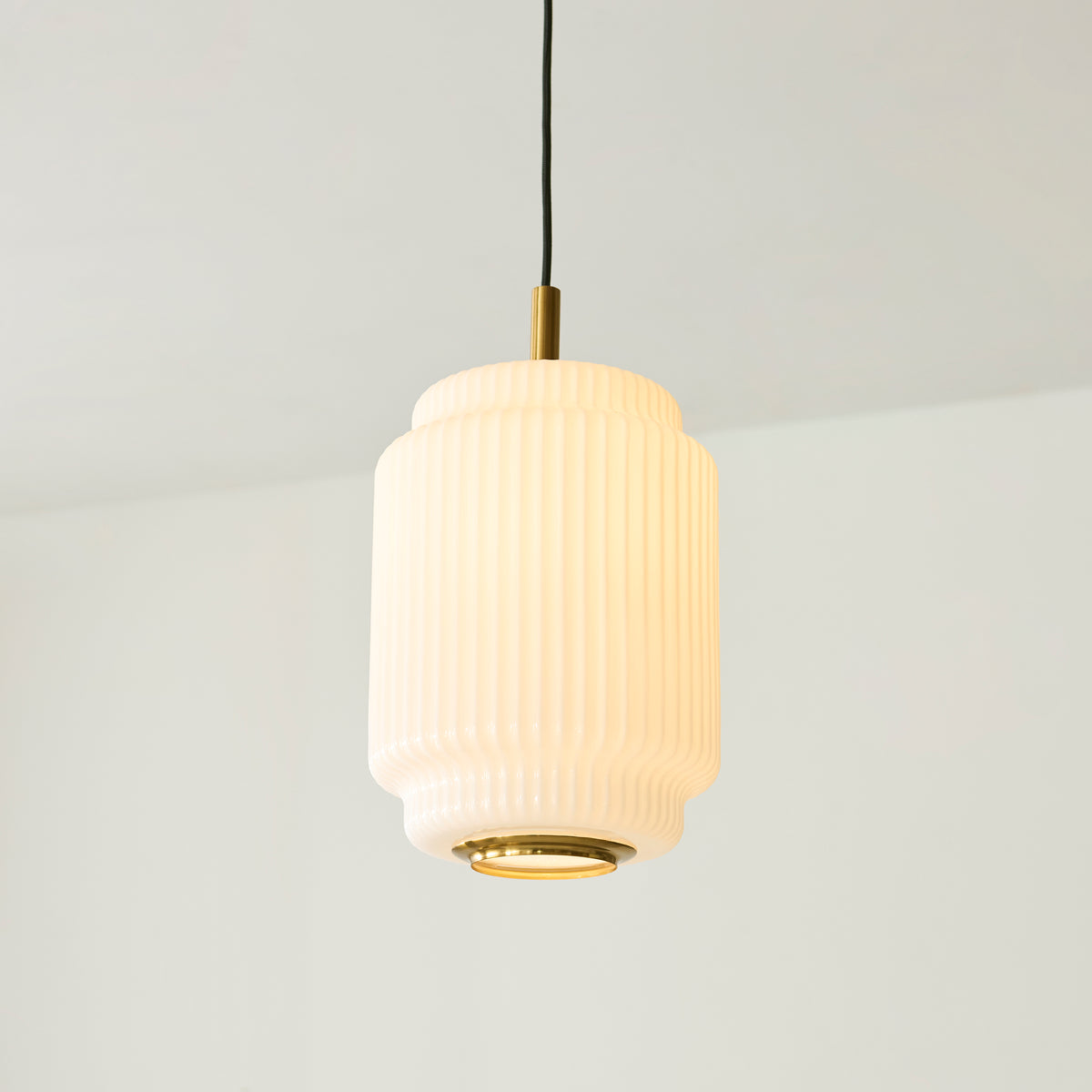 Lit Evora pendant showing the ribbed opal glass cylinder and brass diffuser beneath