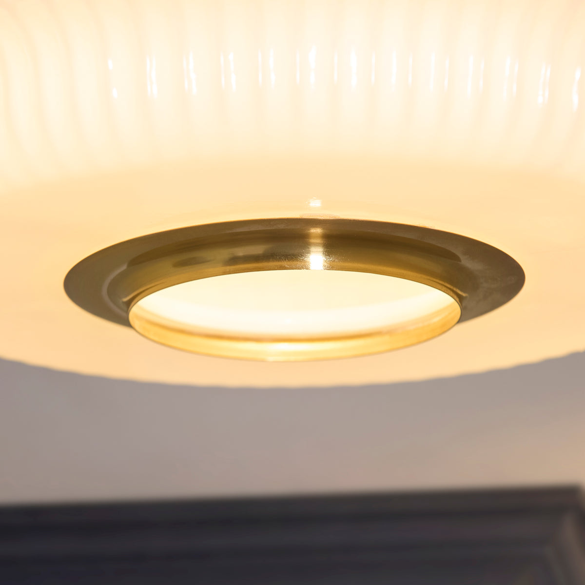 Underside detail of the Evora flush light's brass ring and illuminated opal glass diffuser