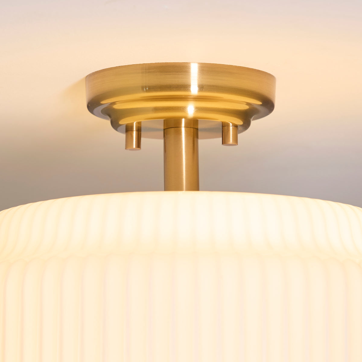 Detail of the Evora flush light's aged brass ceiling plate above the ribbed opal glass shade