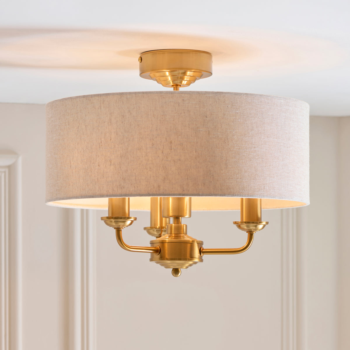 Angled view of the Highclere brass three-arm fitting beneath its natural linen drum shade