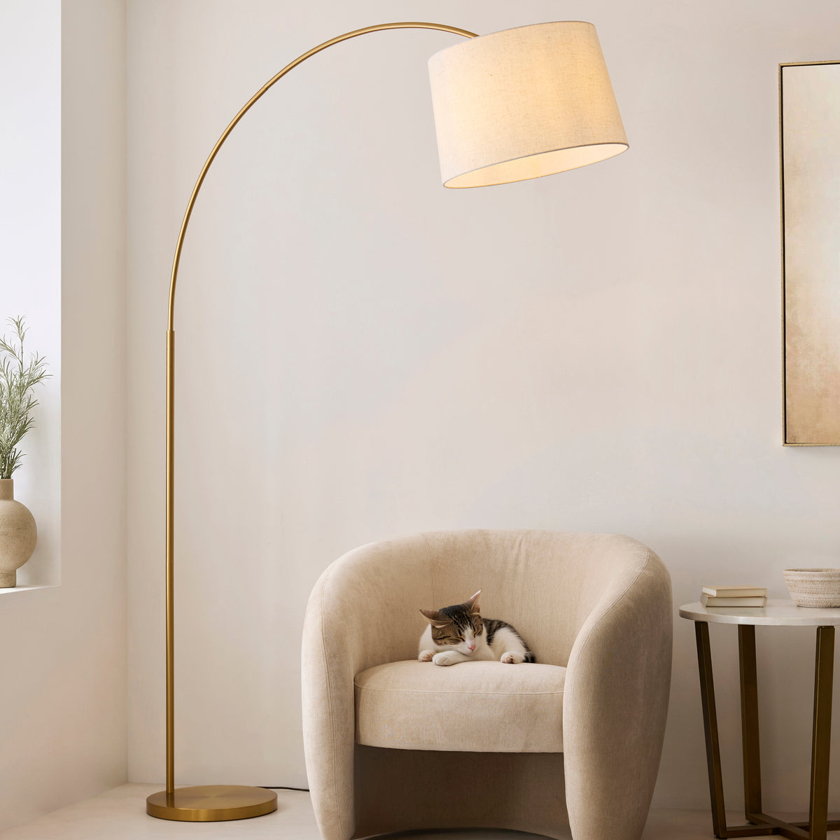 Carlson XL brass arc floor lamp lit over a cream boucle armchair with a cat curled up