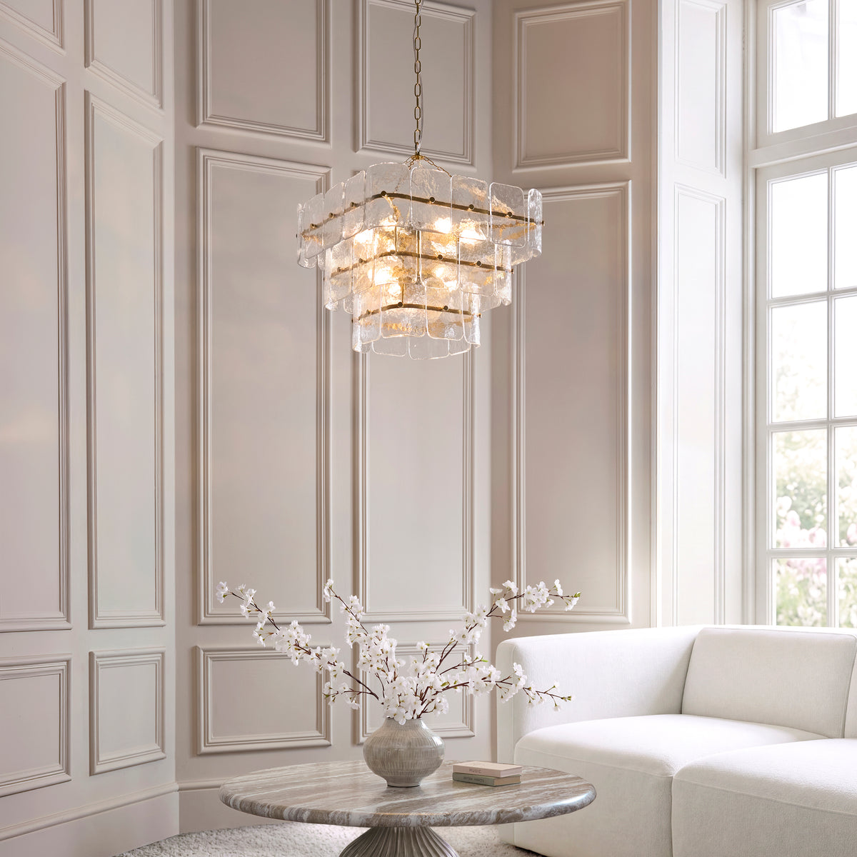 Venice glass chandelier lit above a cream sofa and marble table in a panelled living room