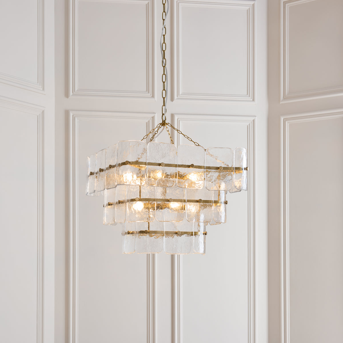 Venice aged brass chandelier glowing against pale panelled walls in an elegant hallway