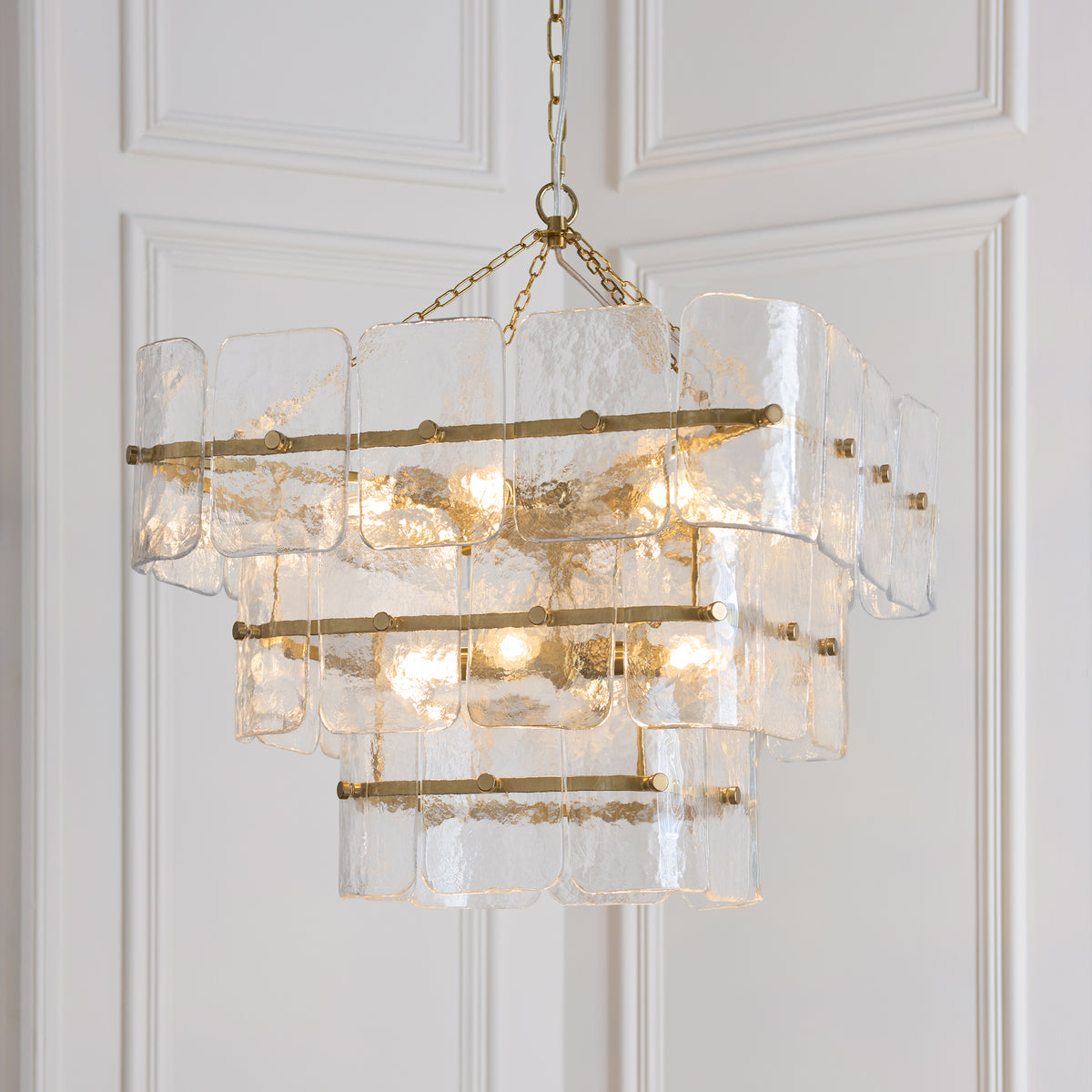 Angled view of the Venice chandelier's tiered clear glass panels held by aged brass bars