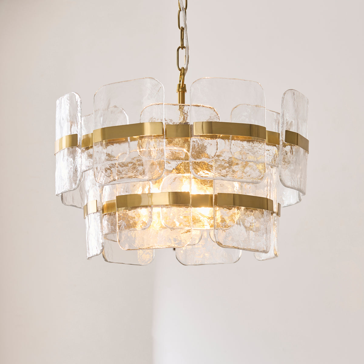Ancara brushed brass pendant glowing with warm light against a soft grey wall