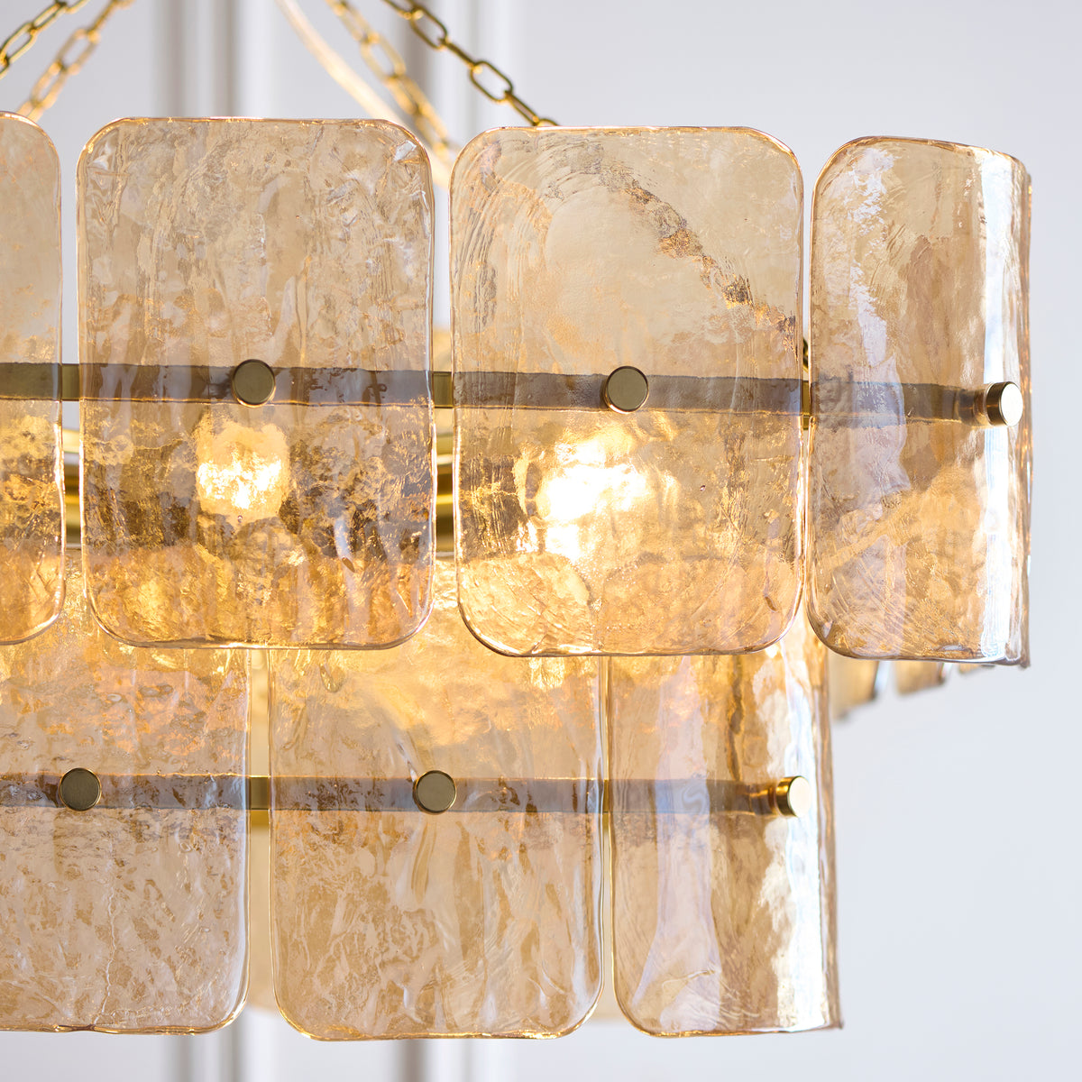 Detail of overlapping champagne textured glass panels with brass studs on the Venice chandelier