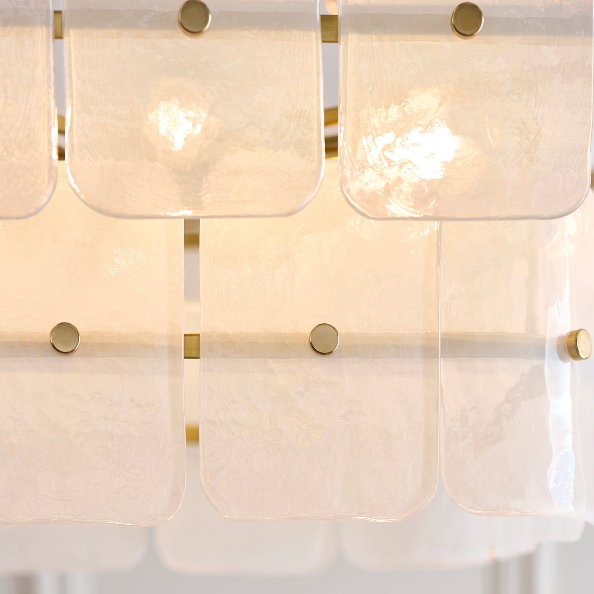Detail of the Venice chandelier's overlapping textured glass panels with brass studs and lit lamps