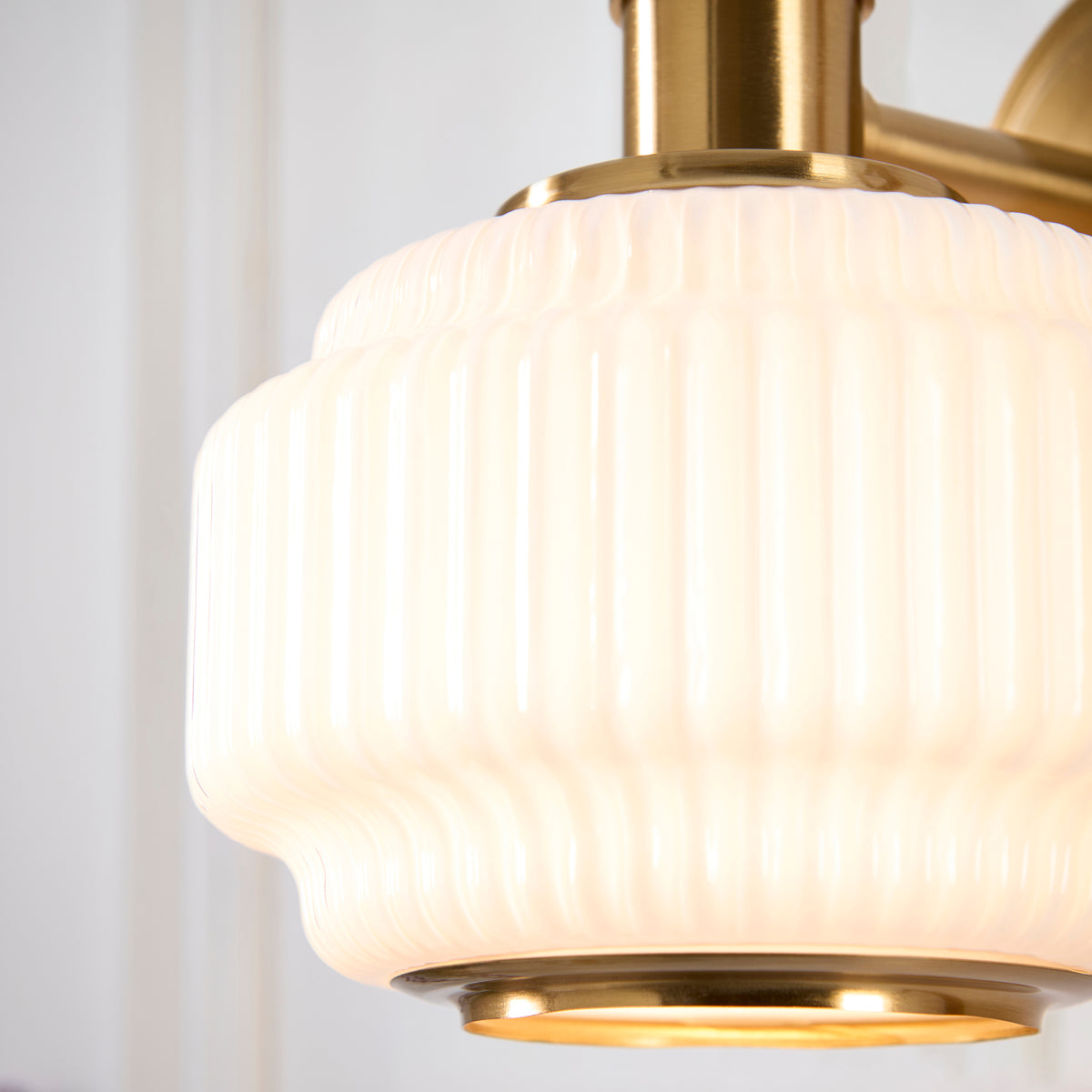 Close-up of the Evora wall light's stepped ribbed opal glass shade and brass base ring