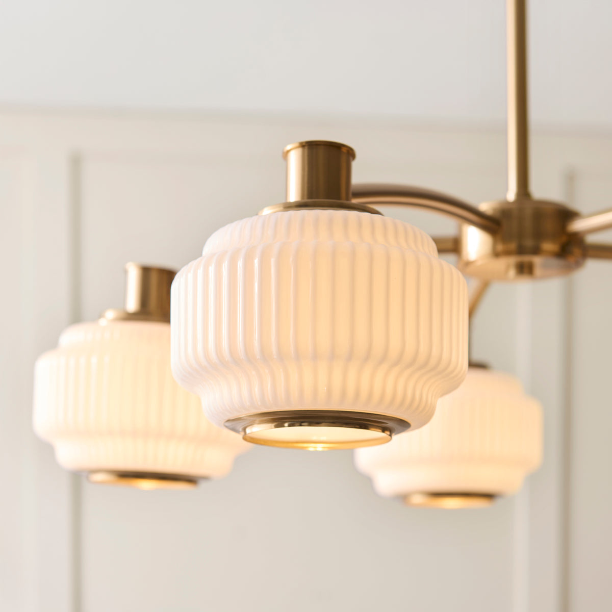 Close view of the Evora chandelier's ribbed opal glass shades with brass collars and trim rings
