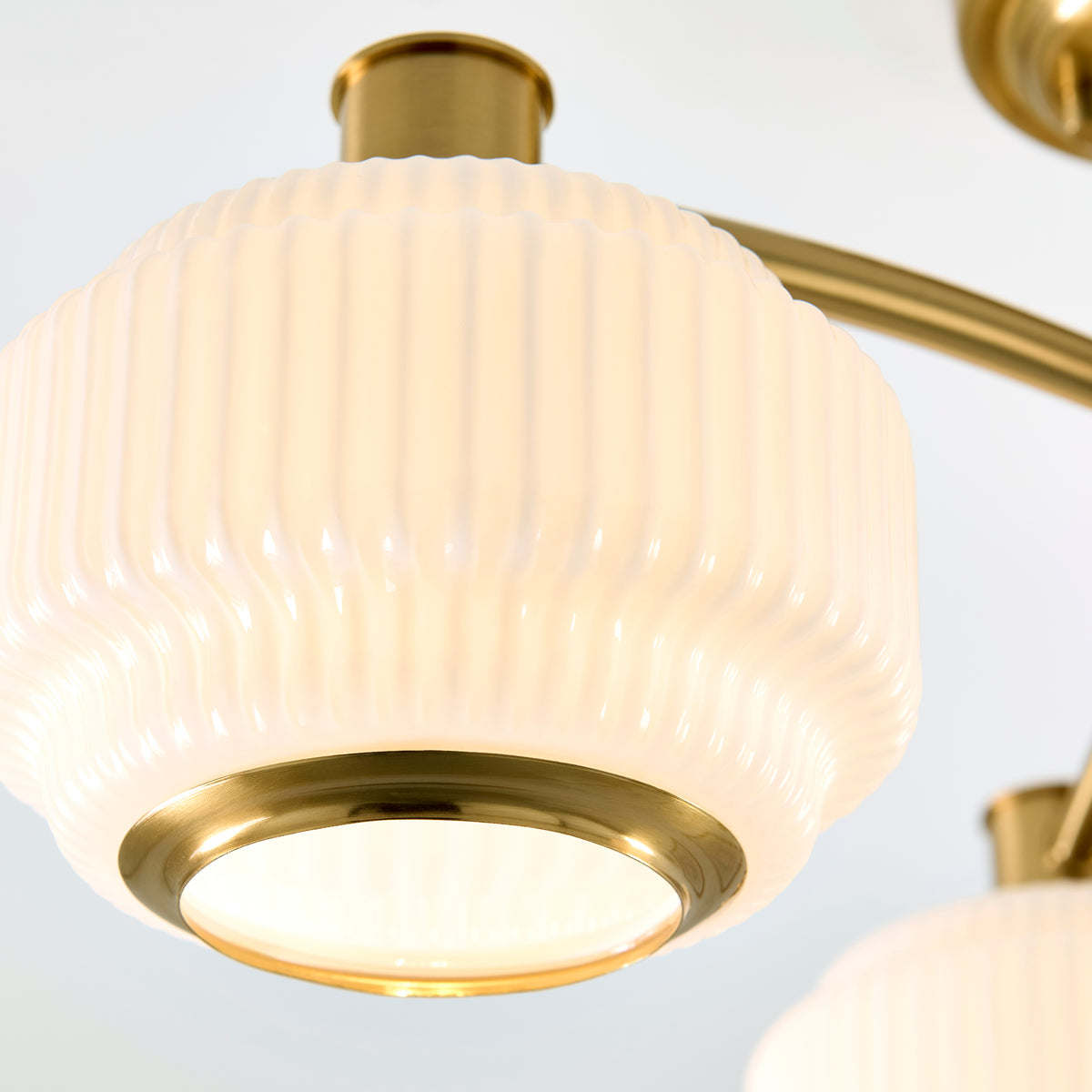 Detail of one ribbed opal glass shade on the Evora ceiling light with brass trim ring lit