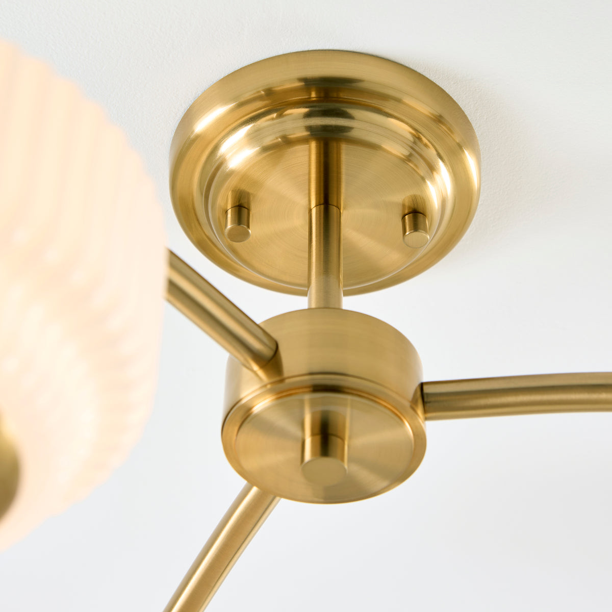 Brushed brass ceiling plate and short stem of the Evora semi flush light on a white ceiling