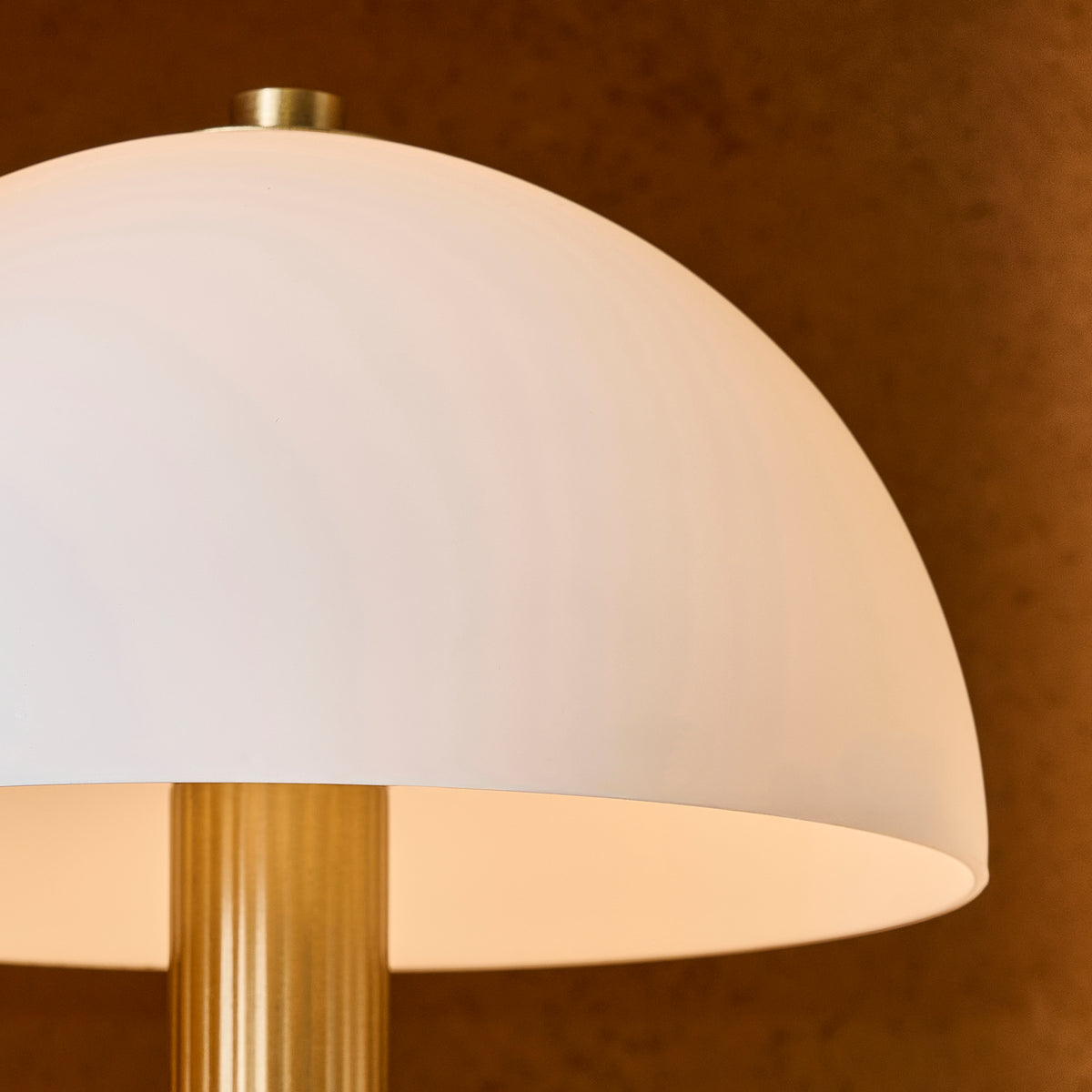 Detail of the Bridport lamp's white glass dome shade and ribbed warm brass stem casting a soft glow