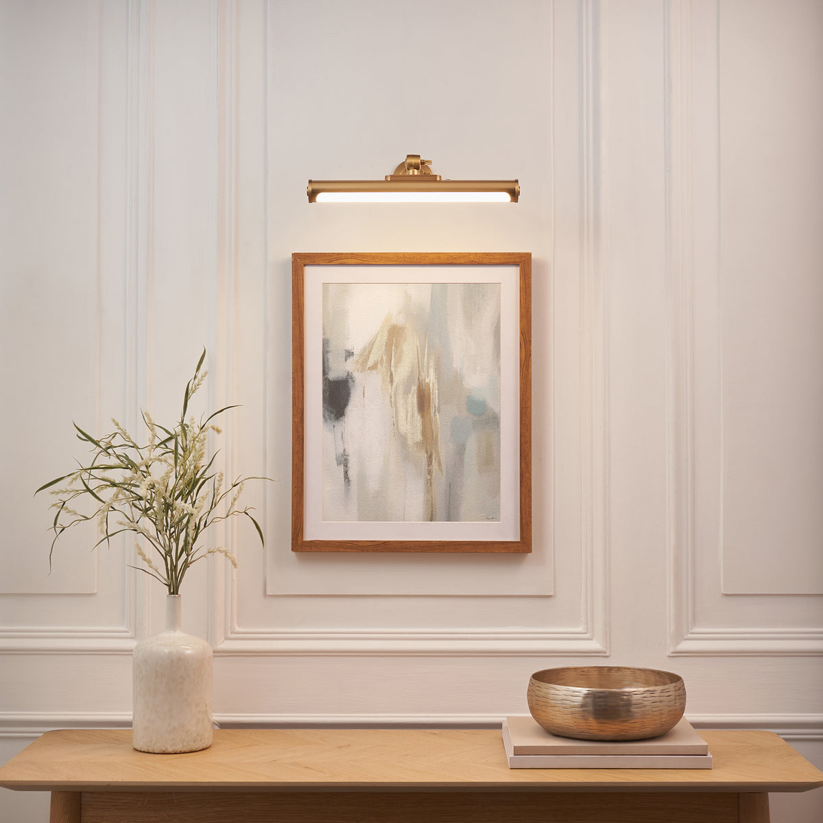 Kas brass picture light illuminating a framed abstract print above a console with vase and brass bowl