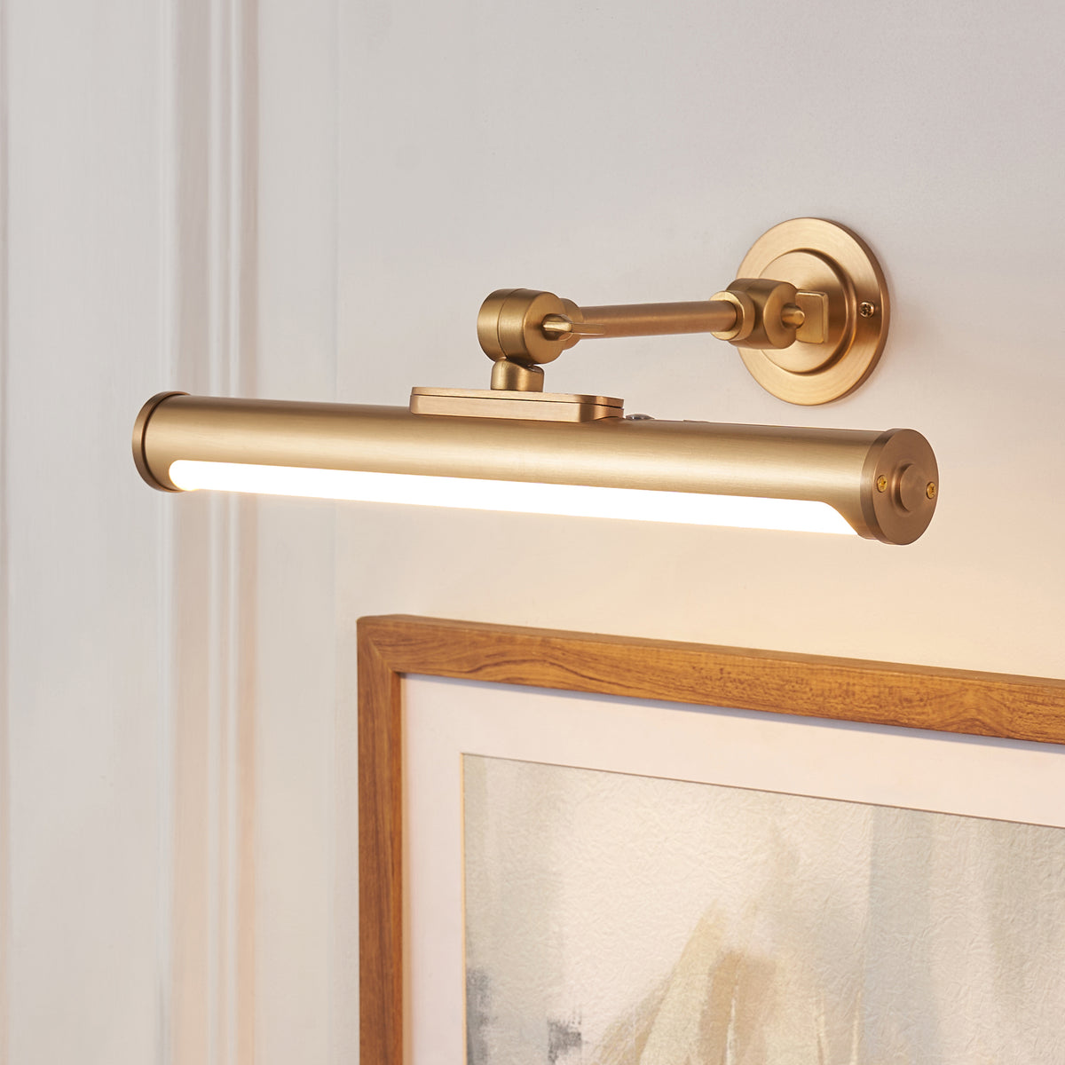 Kas picture light in warm brass mounted above a wooden picture frame, LED strip glowing