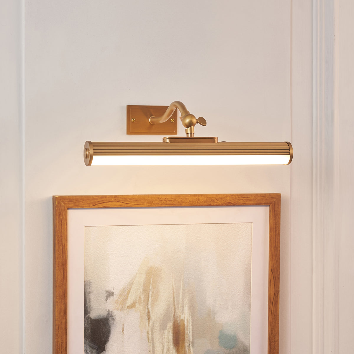 Kindos warm brass picture light glowing above an oak-framed abstract artwork on a panelled wall