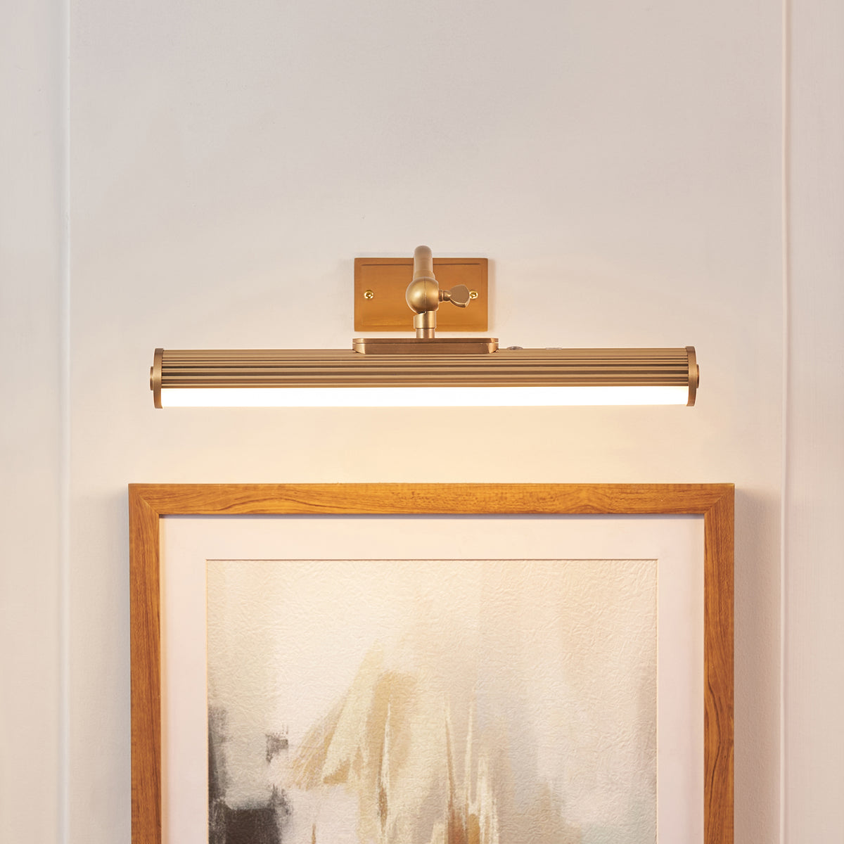 Ribbed brass Kindos picture light casting warm light over an oak-framed abstract print