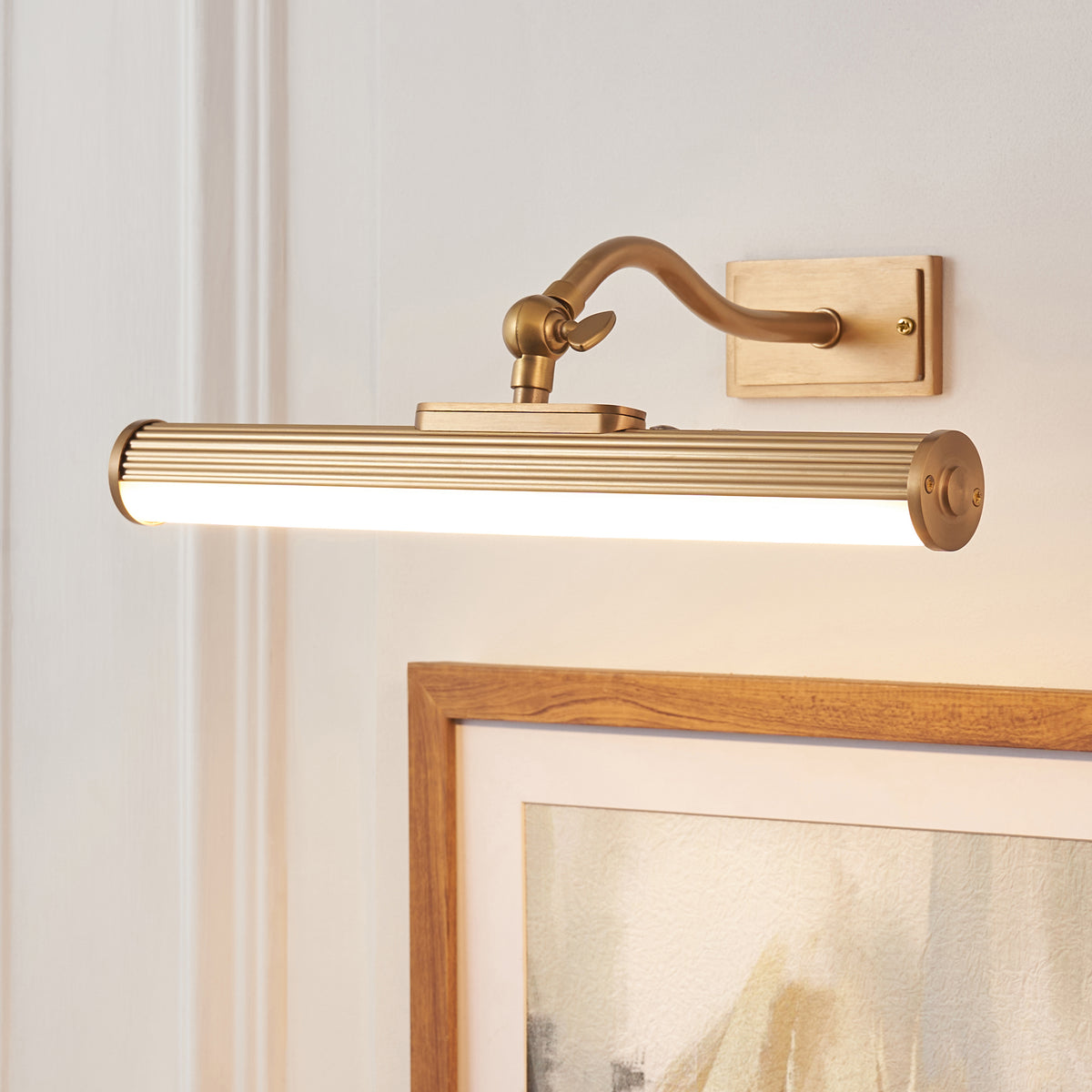 Angled view of the Kindos picture light showing its ribbed brass tube and curved wall-mounted arm