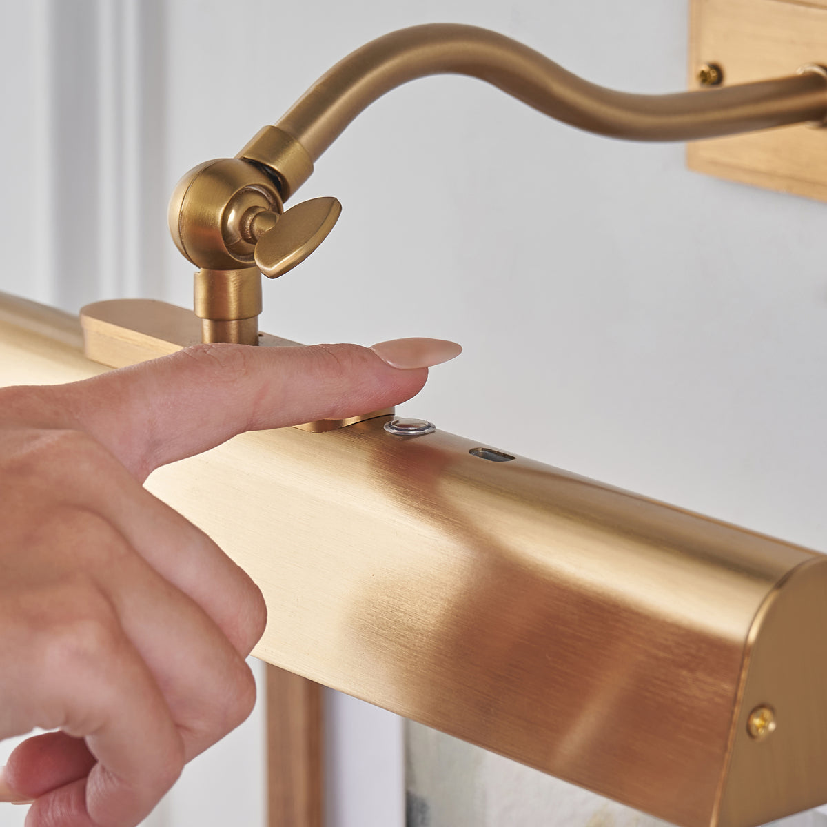 Finger tapping the touch switch on the brushed brass shade of the Lasos picture light