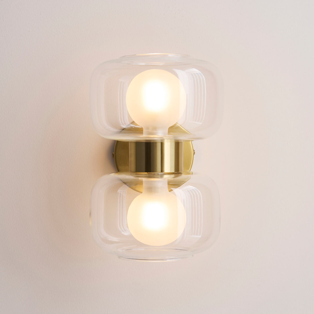 Head-on view of the Rossano wall light's two clear glass shades and frosted globe bulbs