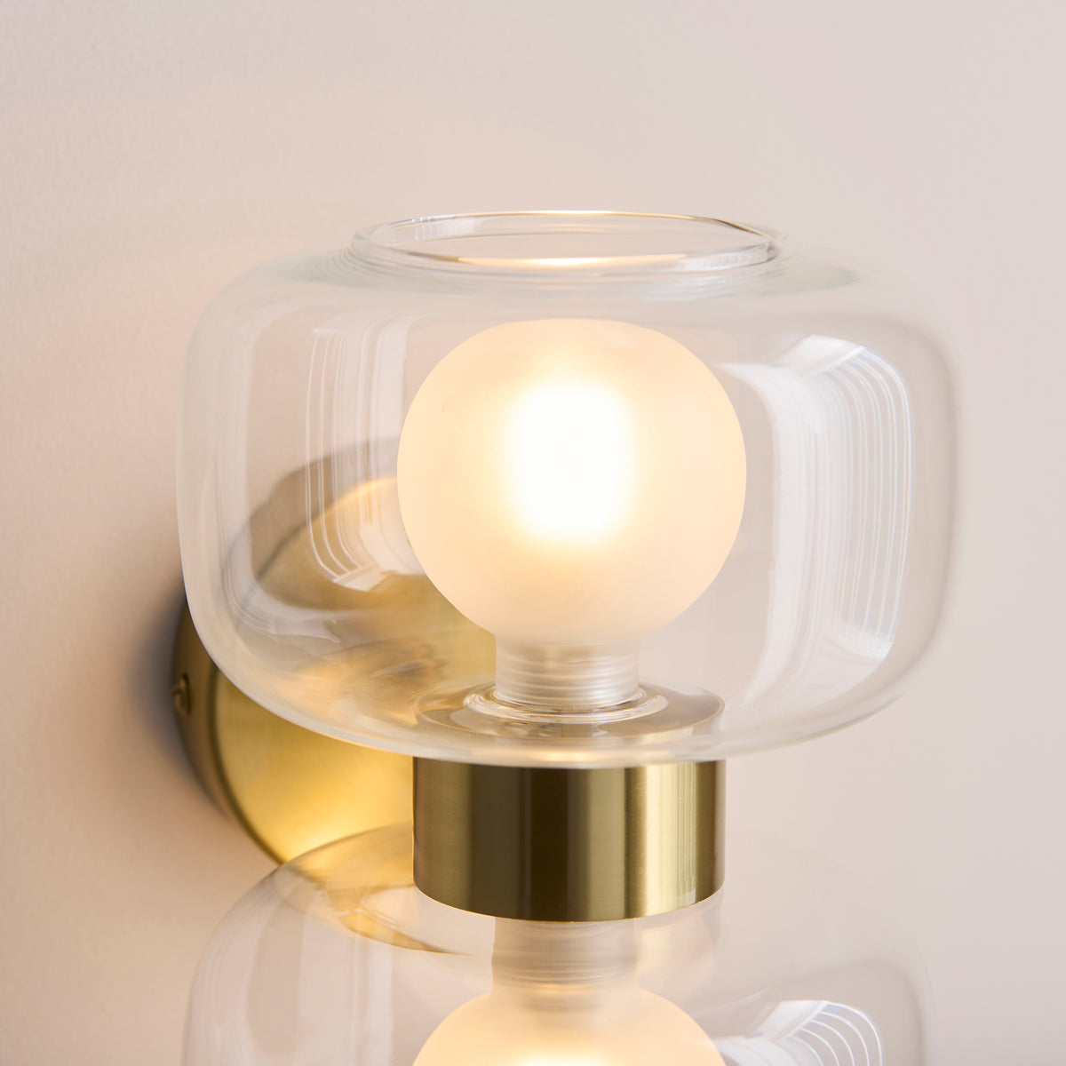 Detail of a single clear glass shade and frosted globe lamp on the Rossano brass wall light