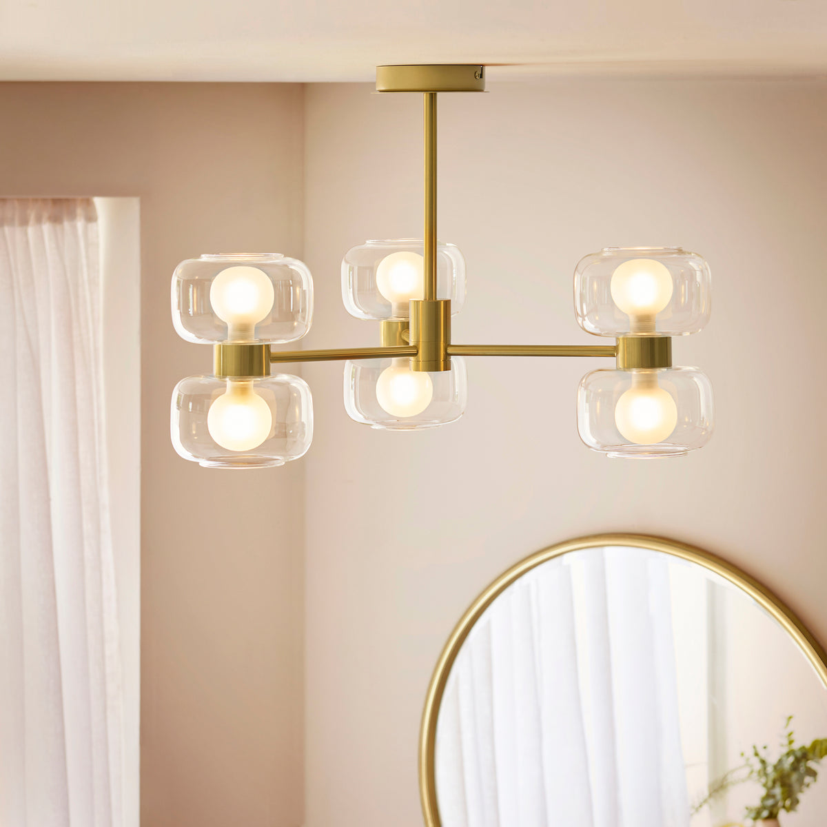 Rossano brass semi-flush ceiling light lit in a bedroom beside a round mirror and curtains