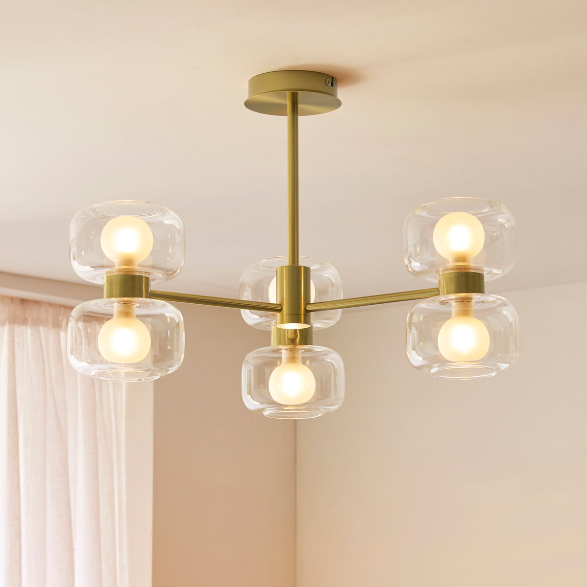 Rossano six-light brass ceiling fitting glowing against a white ceiling near soft curtains